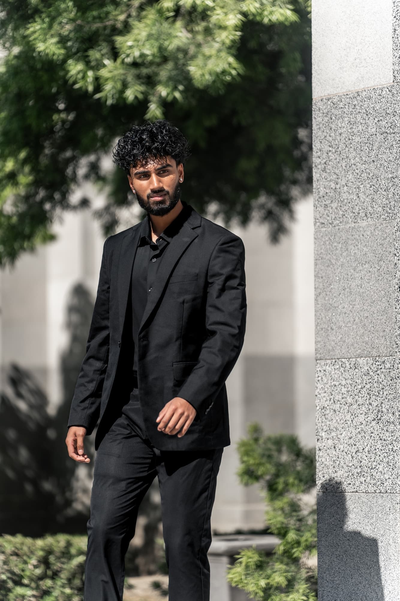 Niv, the photographer and filmmaker behind NIVISION, standing outdoors in a black suit.