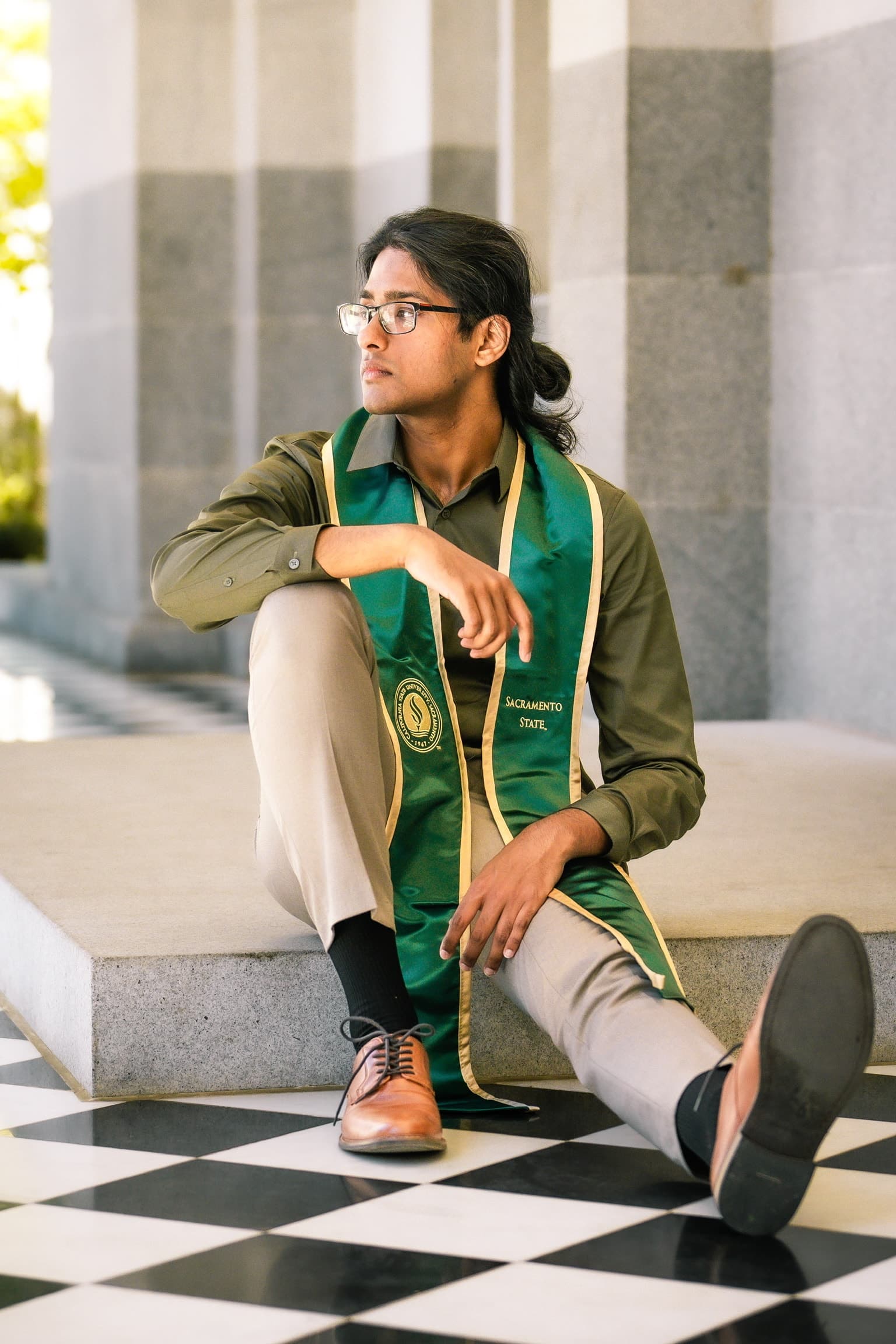 Graduate seated on steps with a green stole and graduation cap