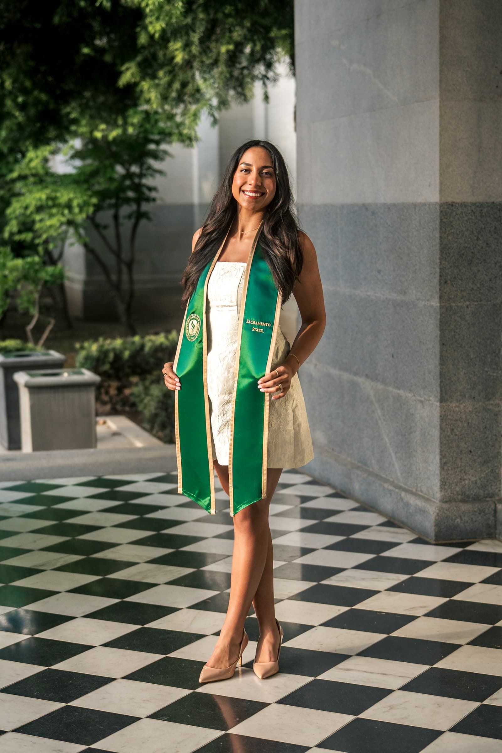 Graduate in a green stole standing on a black-and-white tiled walkway